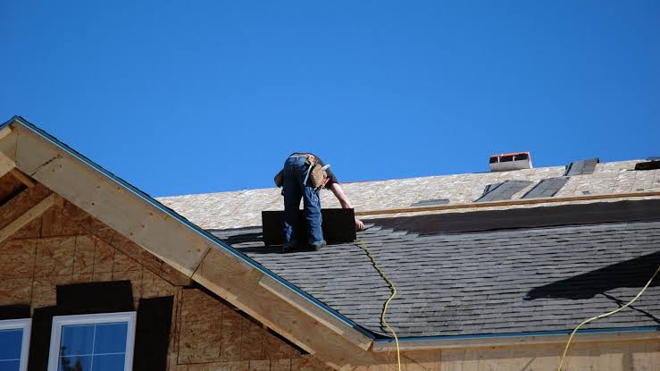 A contractor is performing residential roof repairs using dark asphalt shingles.